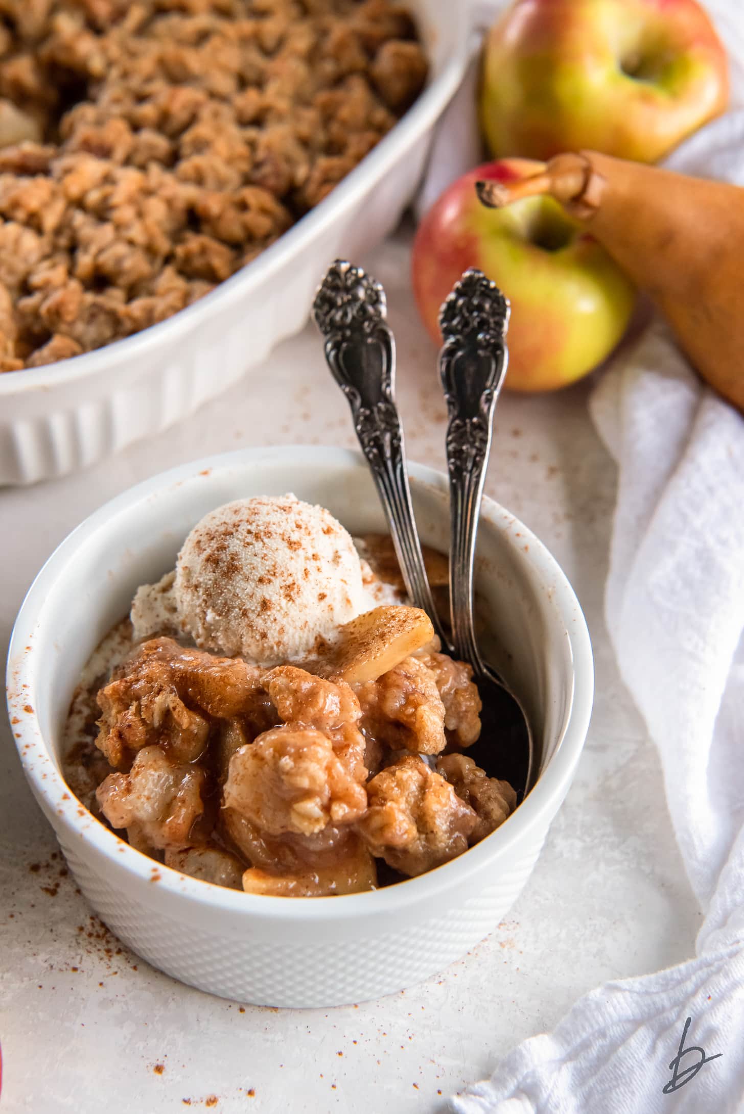 serving of apple pear crisp in a bowl with two spoons.