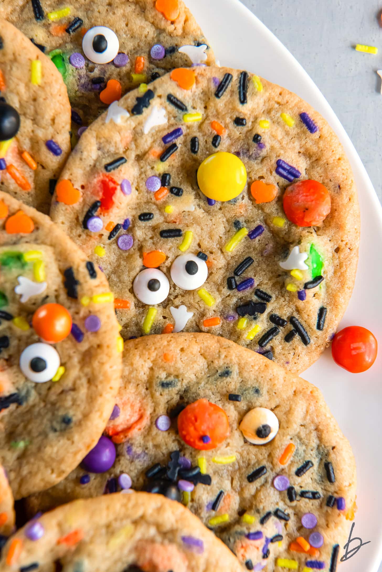 halloween cookie with sprinkles, m&ms and candy eyes on plate with more cookies.