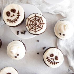 halloween cupcakes with vanilla frosting and decorations to look like skulls, spiderwebs and ghosts.