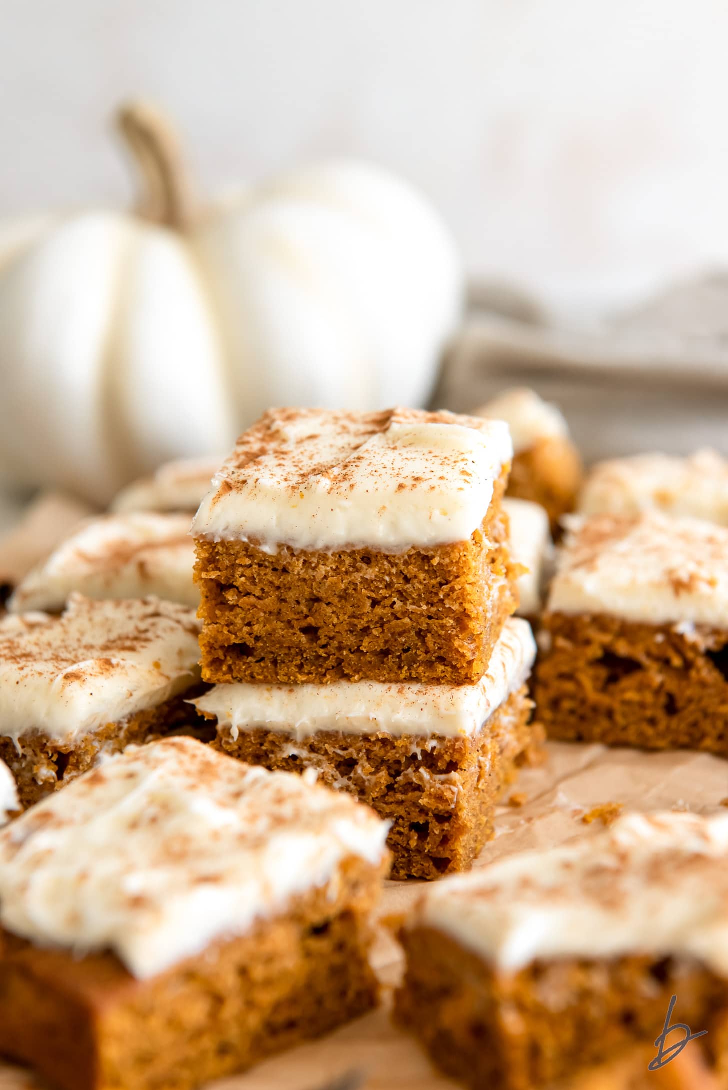 two frosted pumpkin bars stacked in front of small white pumpkin.