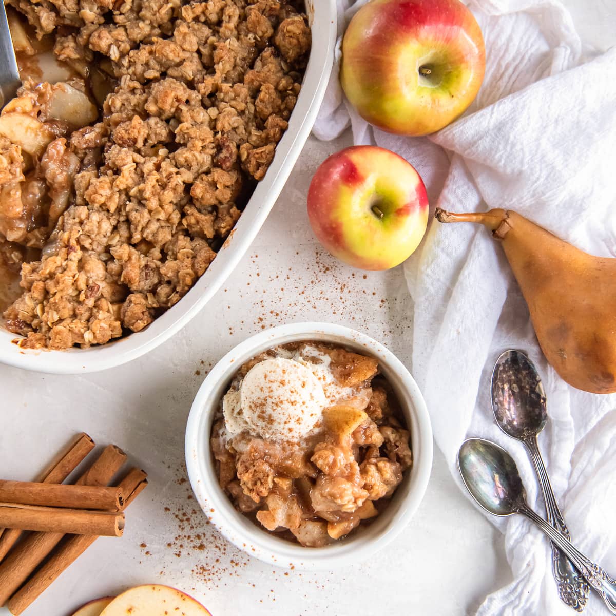 apple pear crisp in a bowl next to baking dish and a couple apples.