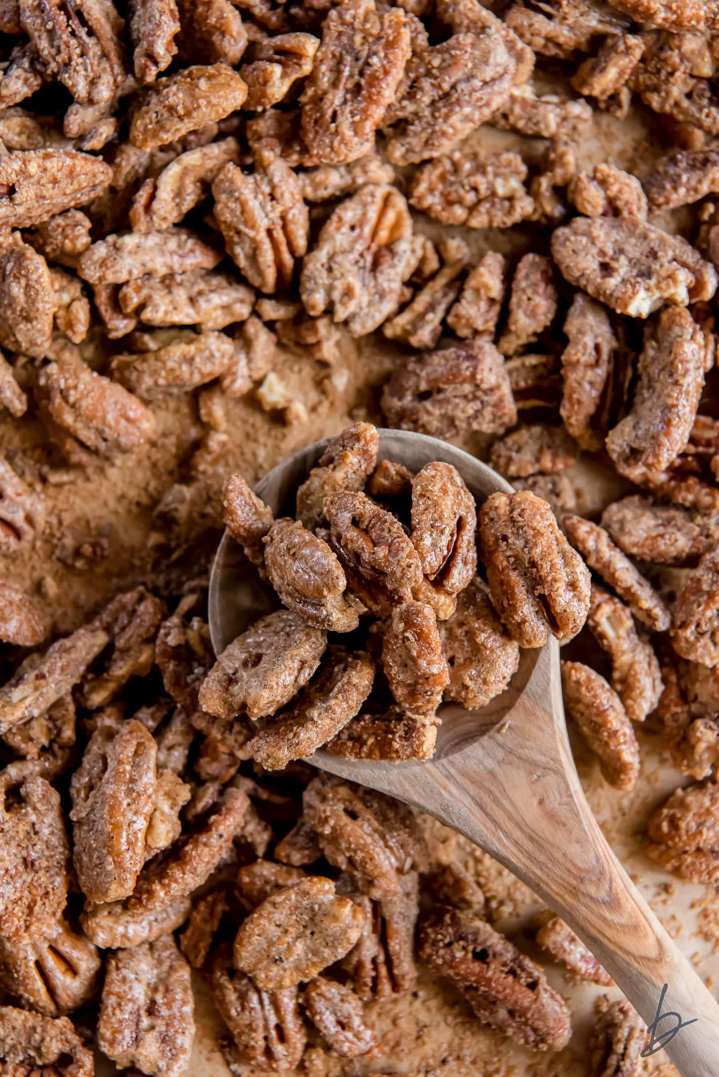 wooden spoon holding spiced pecans on baking sheet with more pecans.