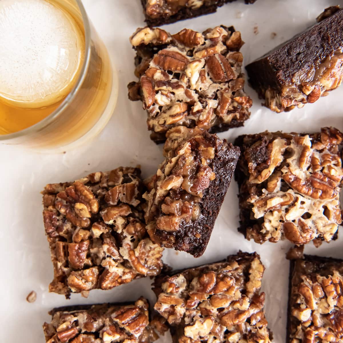 bourbon pecan pie brownie on its side next to more brownies and glass of bourbon.