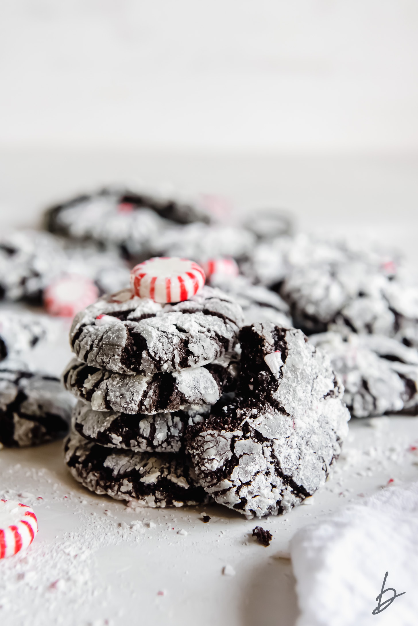 chocolate peppermint crinkle cookie with bite leaning against stack of more cookies with confectioners' sugar.