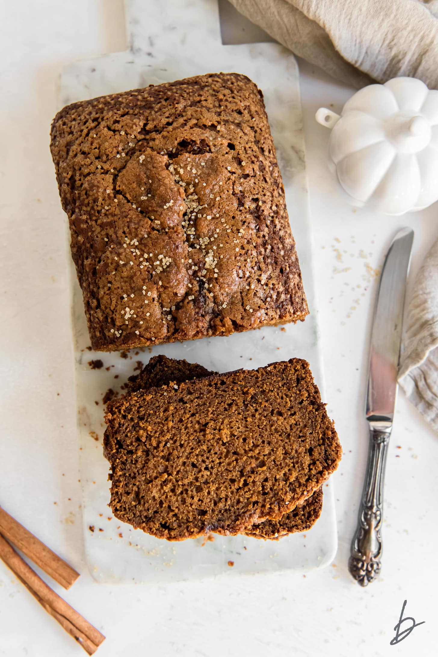 pumpkin gingerbread loaf with slices on a marble slab next to a knife.