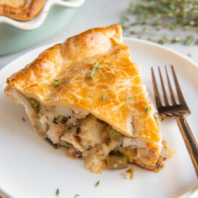 slice of turkey pot pie with filling spilling out on plate with fork.