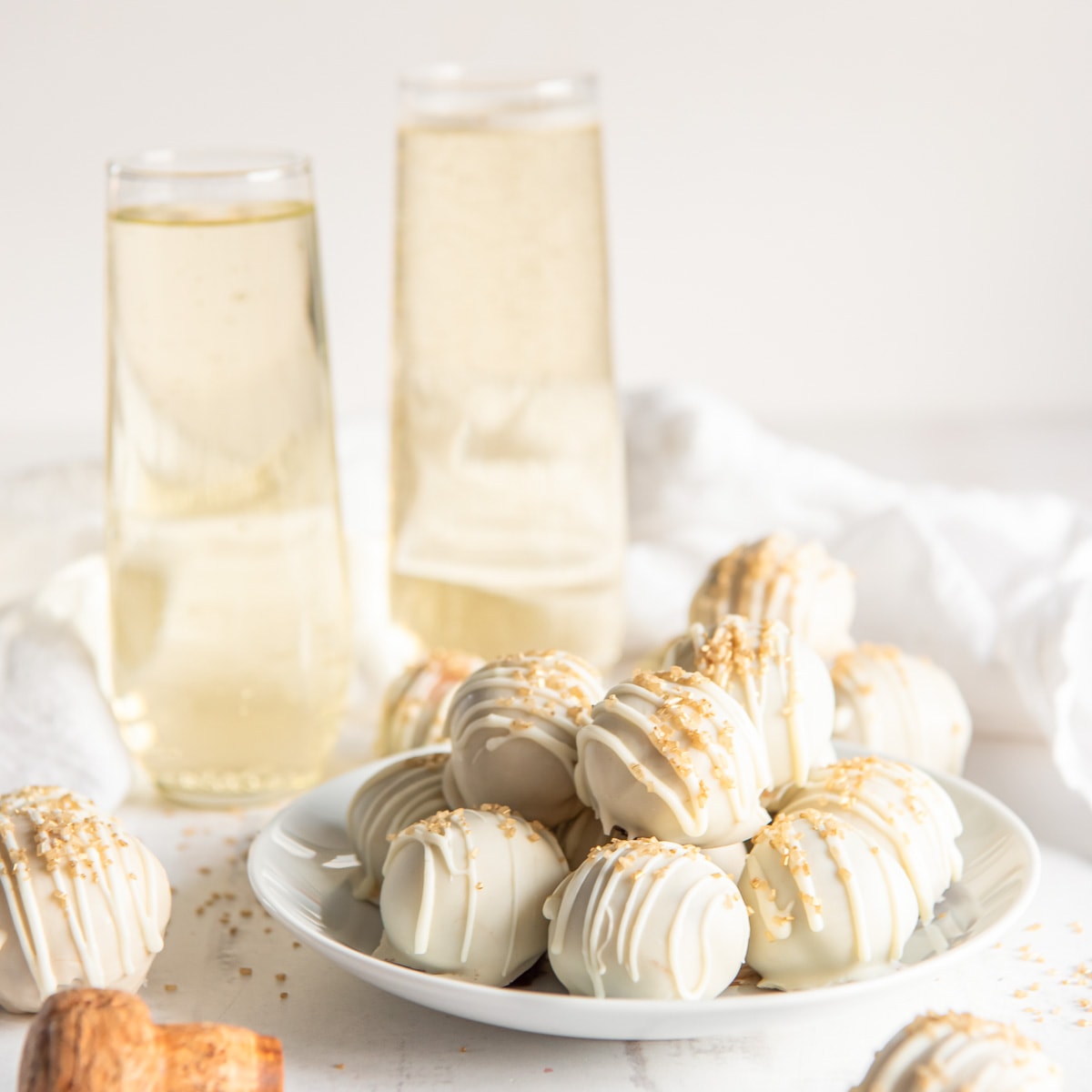 plate of white chocolate covered champagne truffles in front of two stemless champagne flutes.
