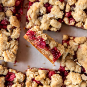 cranberry crumble bar on its side showing layers of crust, cranberry filling and crumb topping.