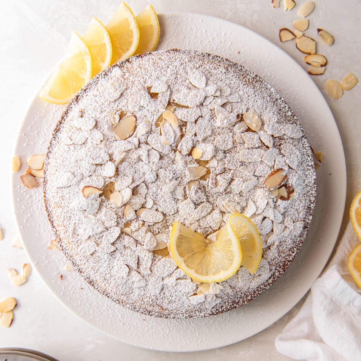 lemon ricotta cake topped with sliced almonds and confectioners sugar.