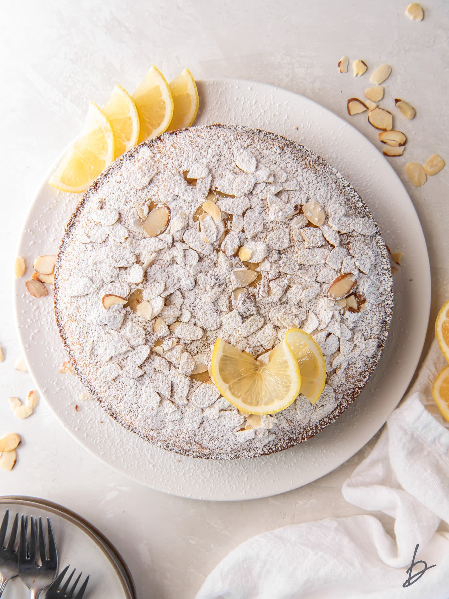 lemon ricotta cake with almonds, confectioners' sugar and lemon wedges as garnish.