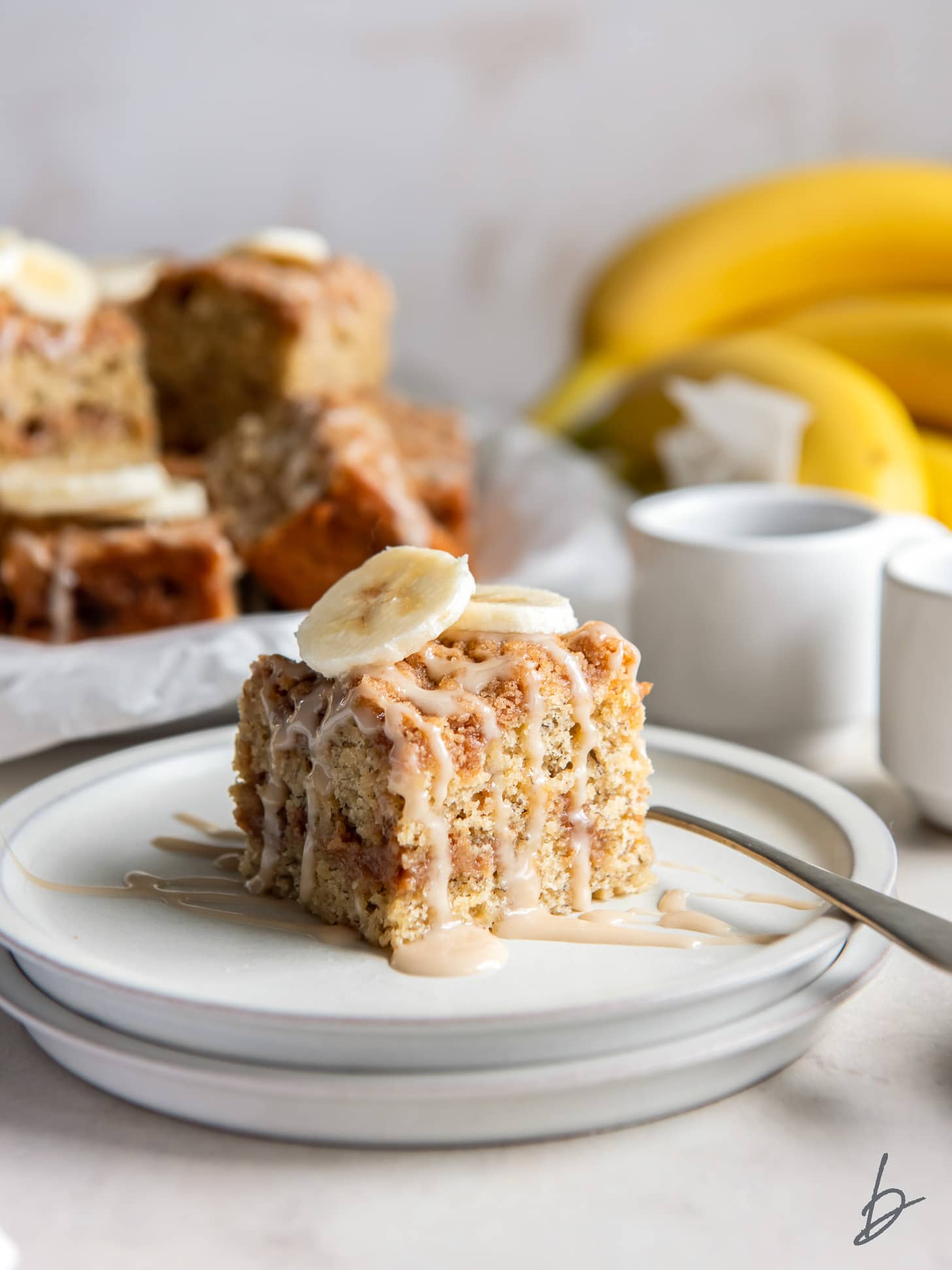 square slice of banana bread coffee cake with icing and banana slice garnish.