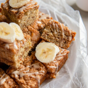 banana coffee cake squares in a pile with glaze and fresh banana slices.