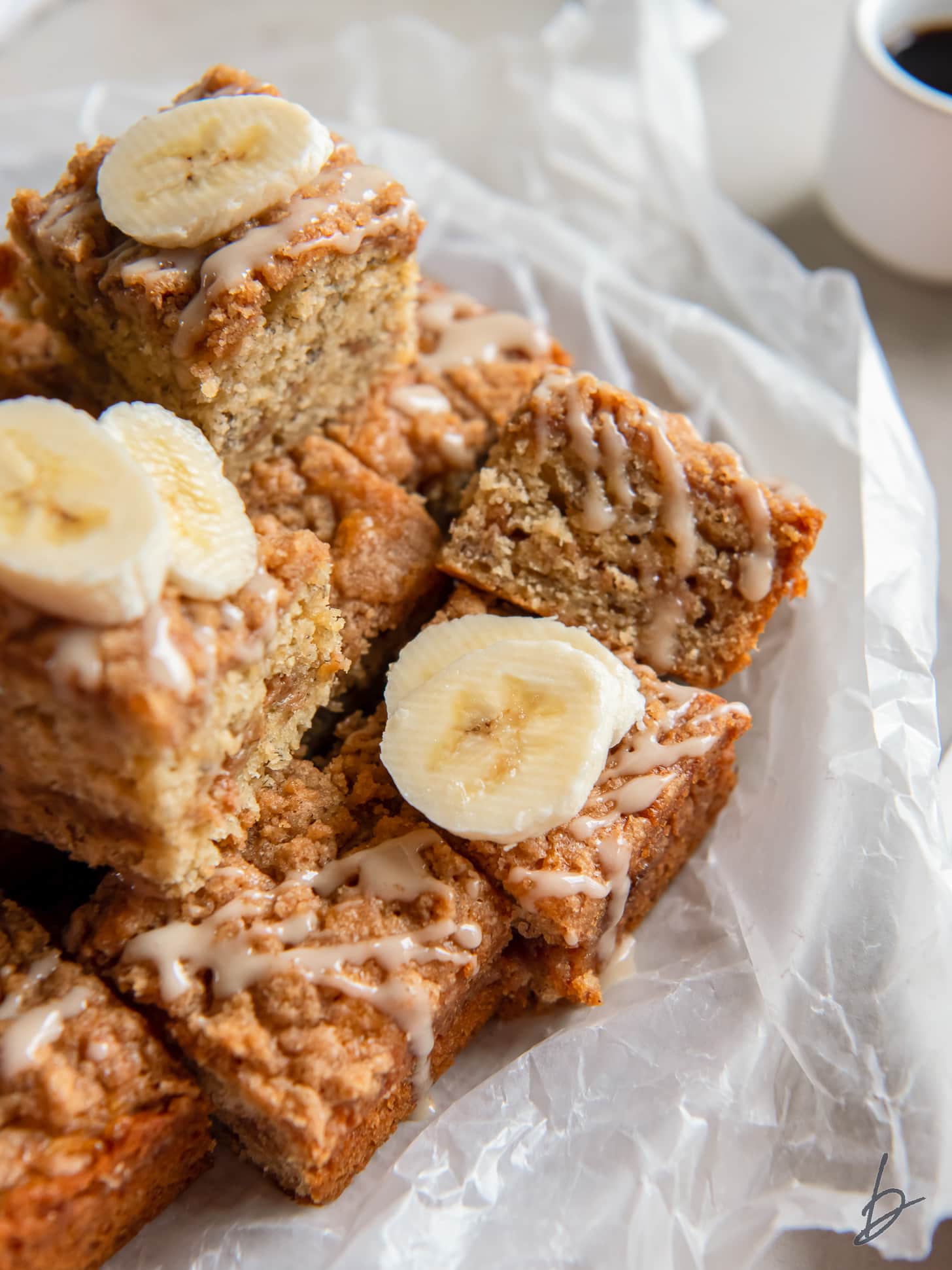 banana coffee cake squares in a pile with glaze and fresh banana slices.