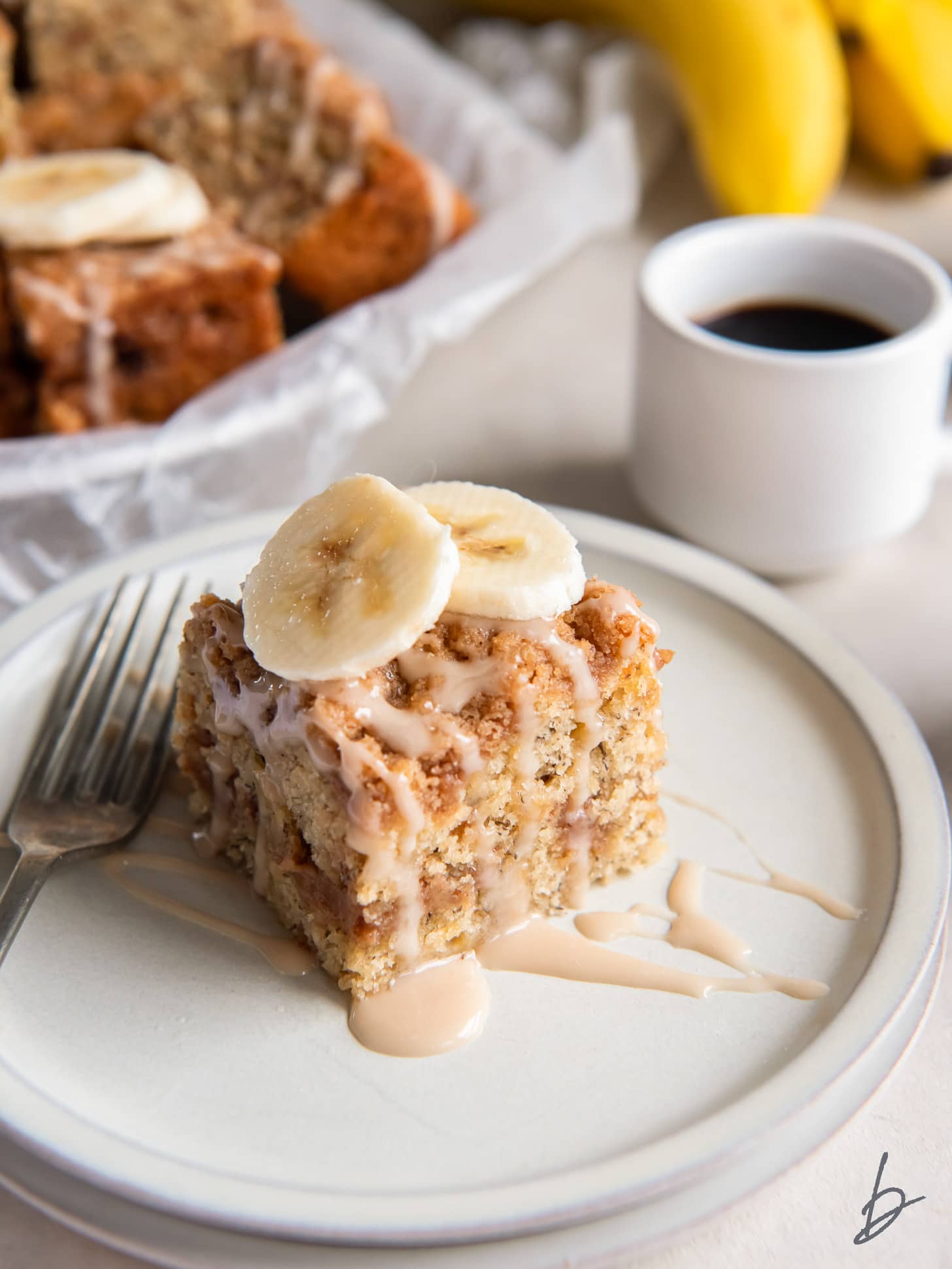 banana bread coffee cake slice with drizzle and banana slices on plate.
