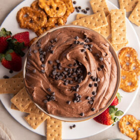 brownie batter dip in a bowl on a plate with graham crackers, pretzel things and strawberries.