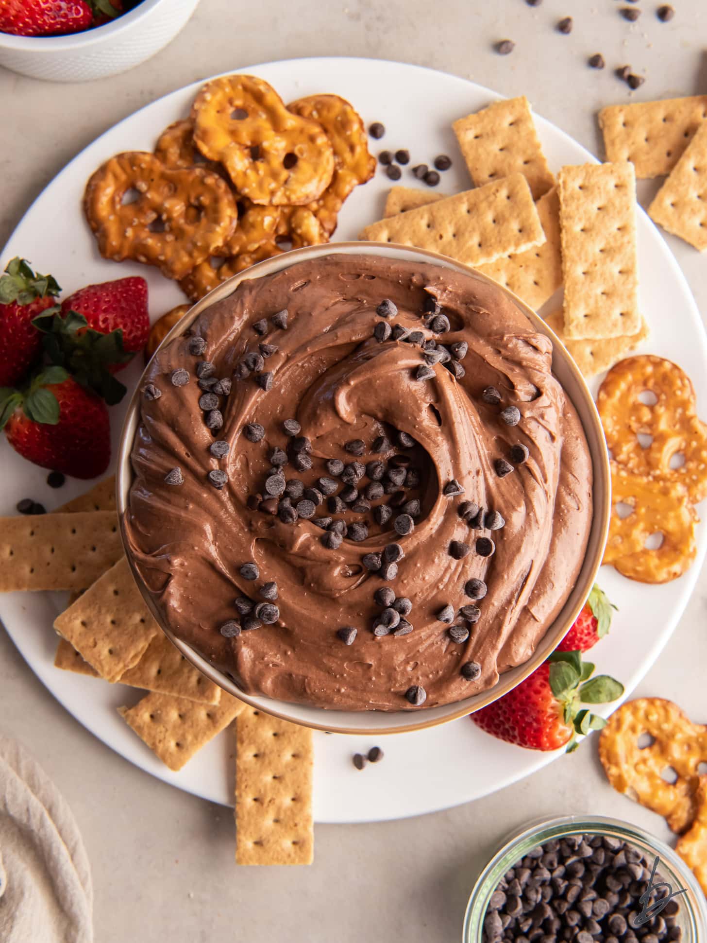 brownie batter dip in a bowl on a plate with graham crackers, pretzel things and strawberries.