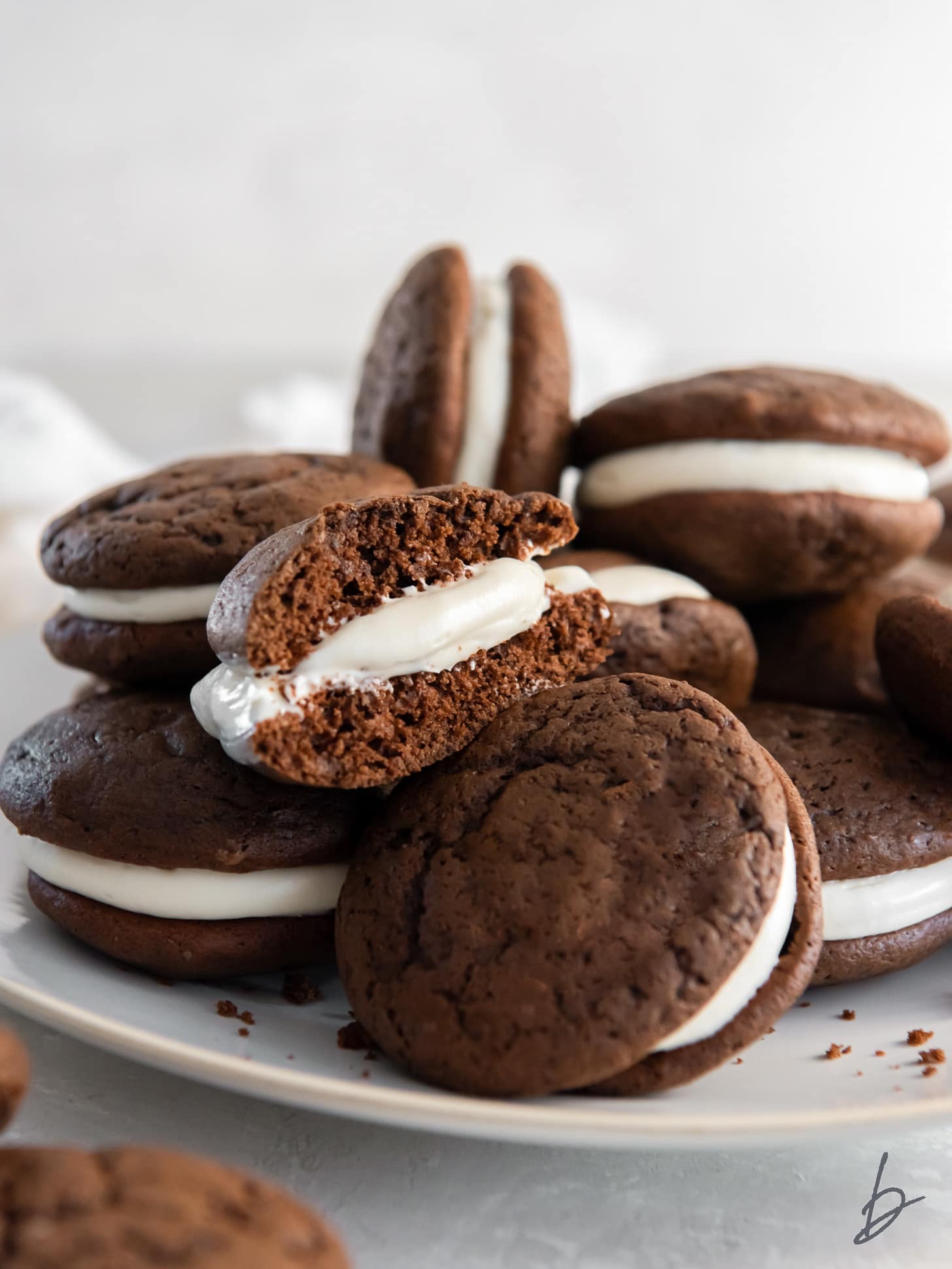 chocolate whoopie pie with bite in pile of more whoopie pies on plate.