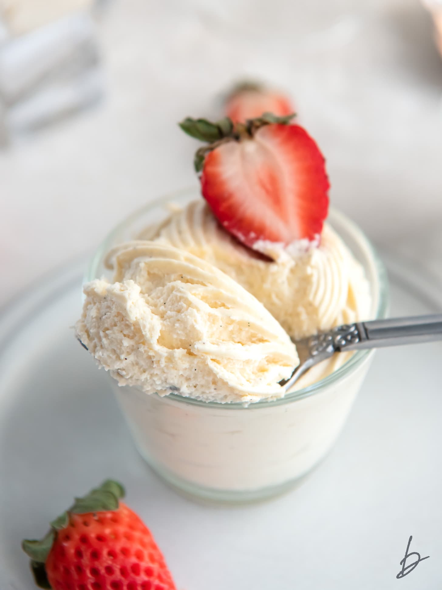 spoon holding bite of vanilla mousse in a jar with strawberry garnish.