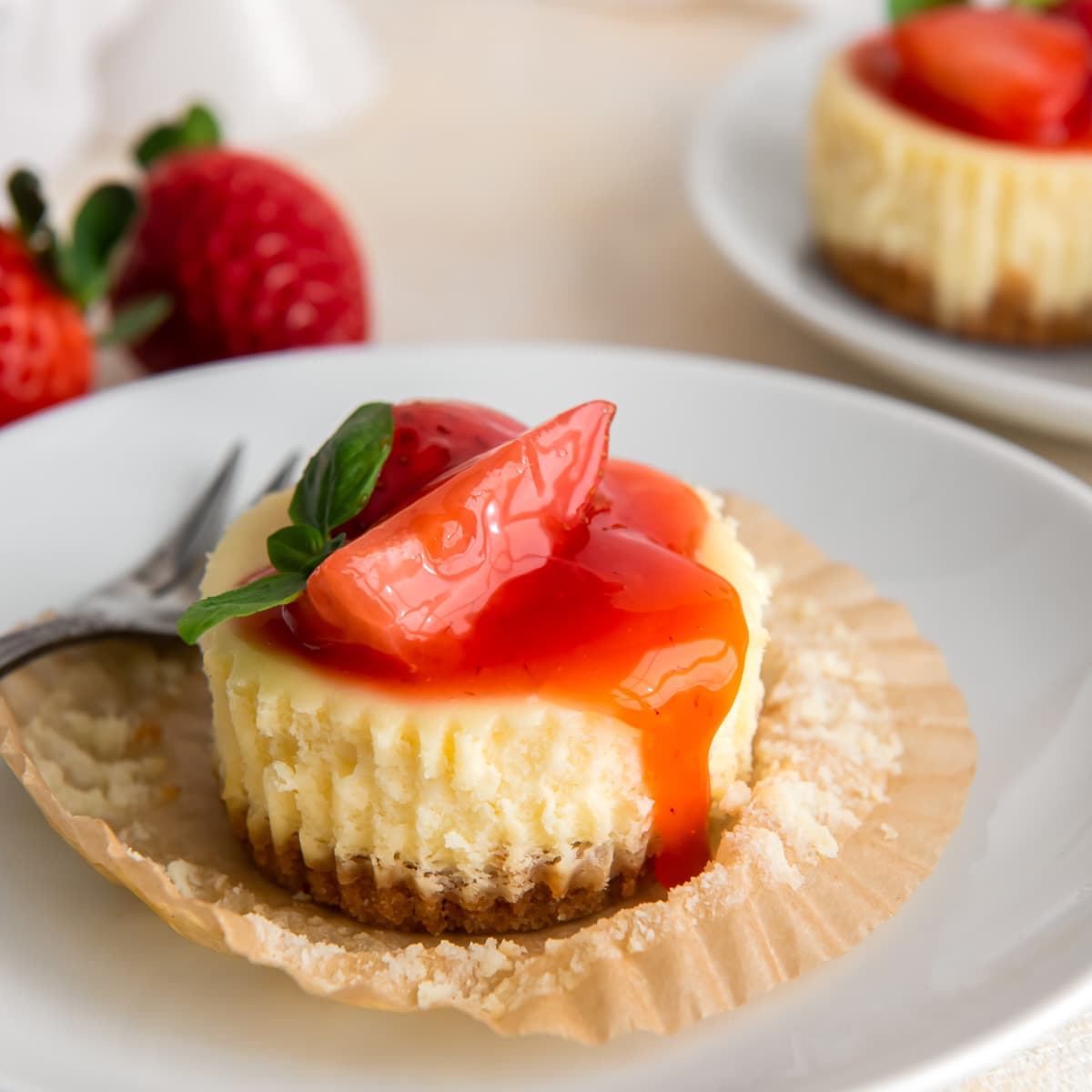 mini cheesecake with strawberry sauce on open paper muffin liner.