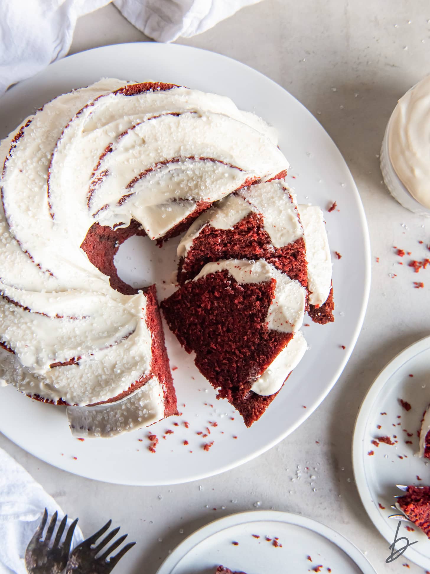 red velvet bundt cake with cream cheese frosting on plate with two slices cut.