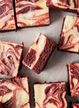 red velvet cheesecake brownie on its side showing layers next to more brownies with marbled tops.