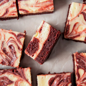 red velvet cheesecake brownie on its side showing layers next to more brownies with marbled tops.