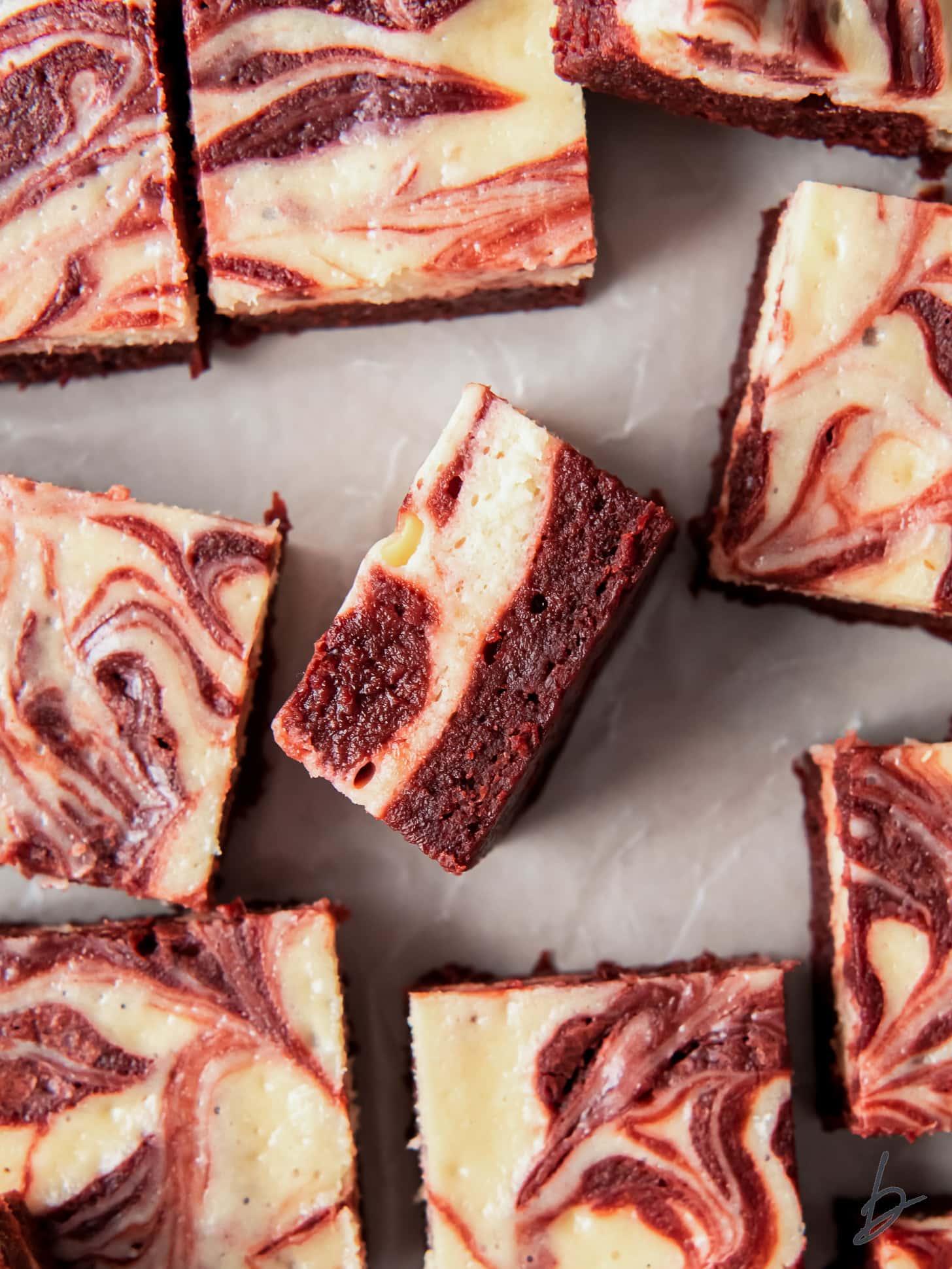 red velvet cheesecake brownie on its side showing layers next to more brownies with marbled tops.
