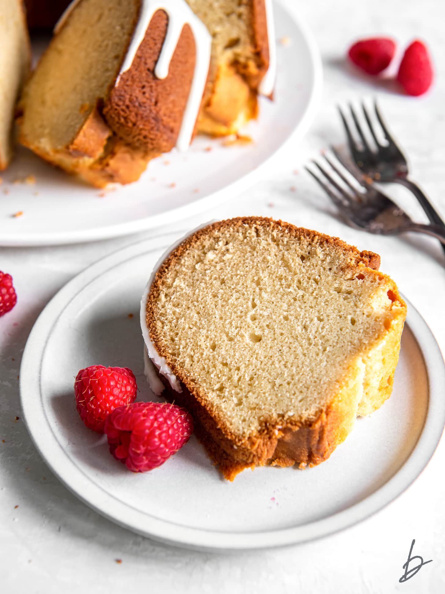 slice of vanilla bundt cake on plate with two raspberries.