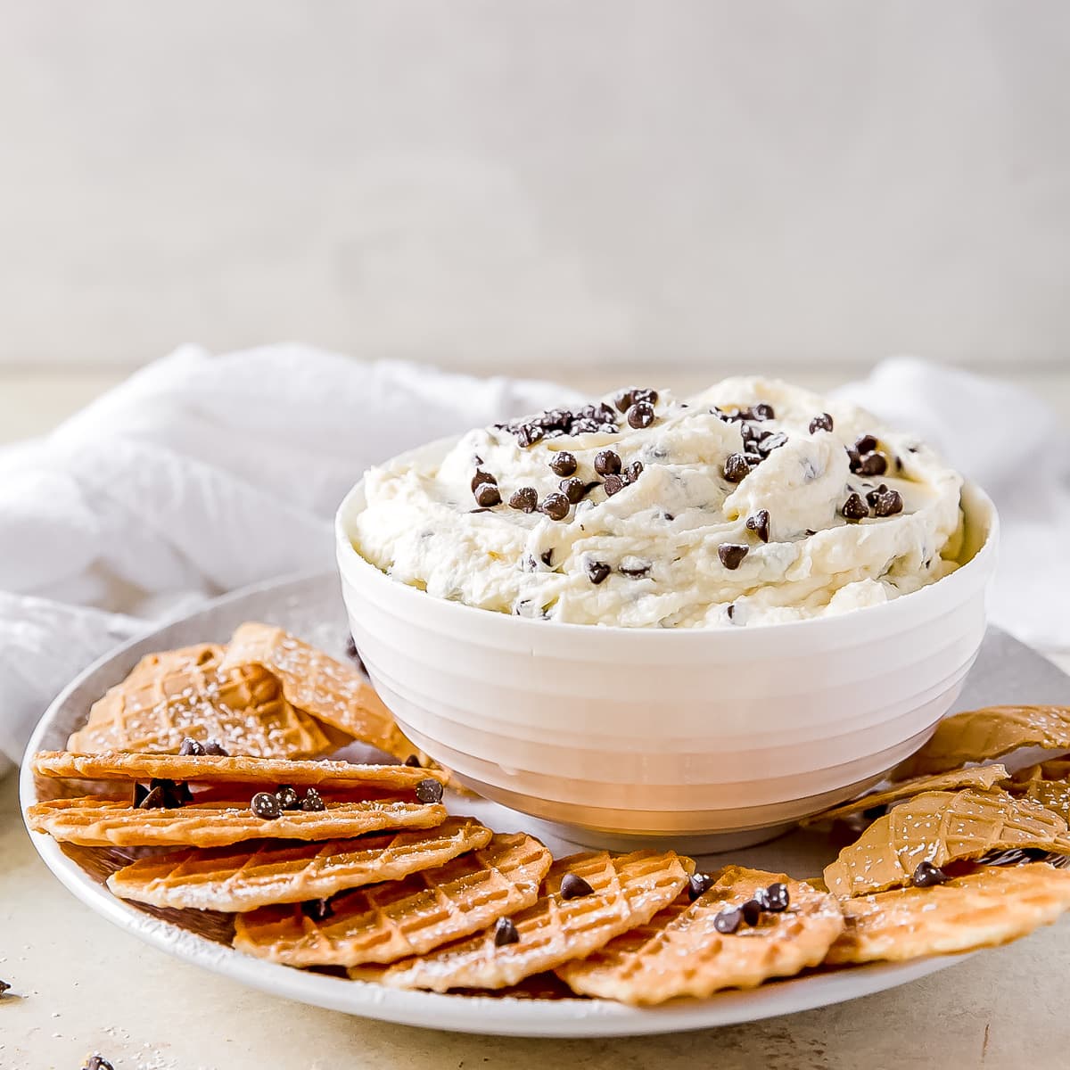 cannoli dip in a bowl on a plate with cannoli chips.