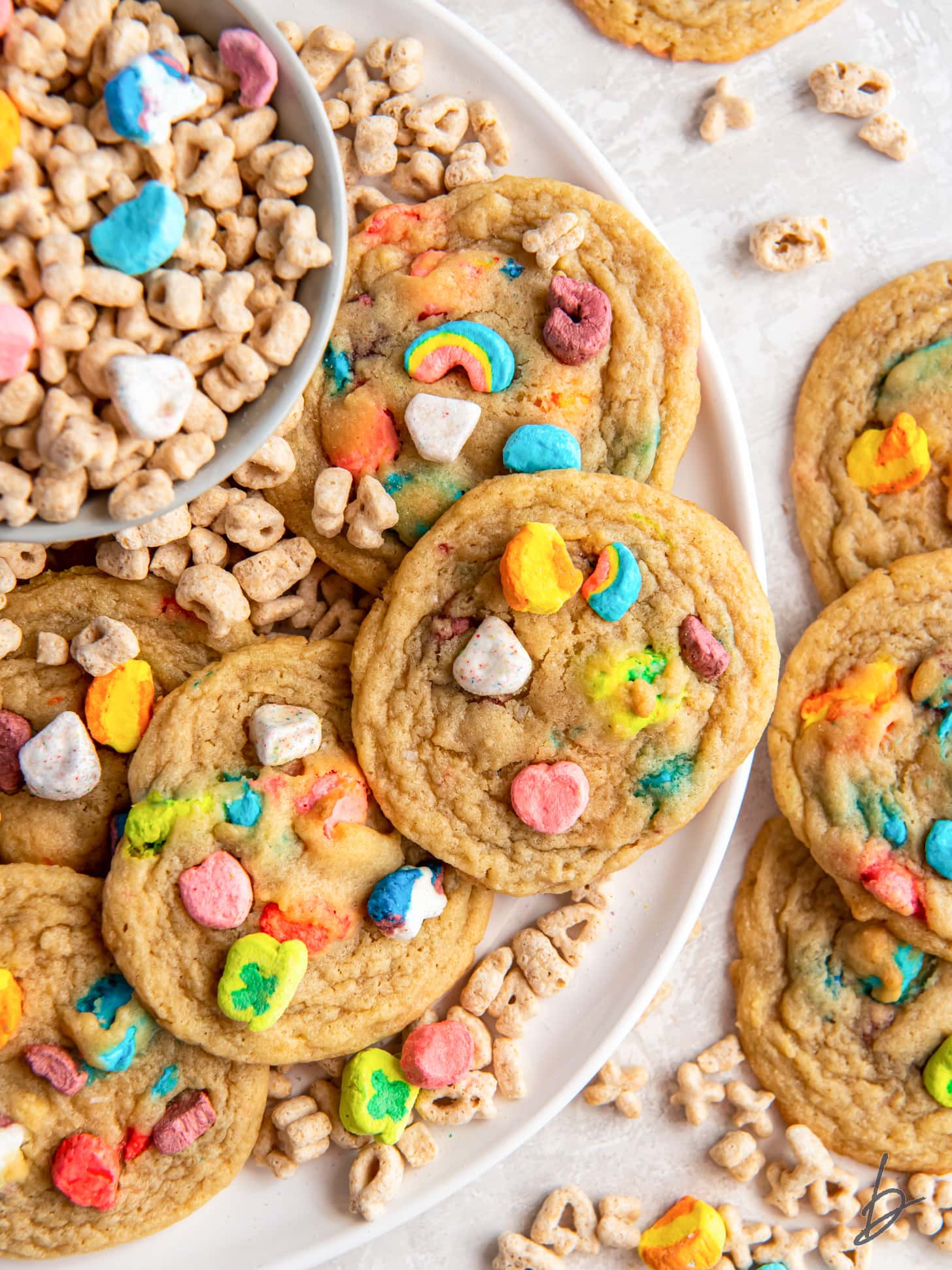 lucky charms cookies on a plate with a bowl of cereal.