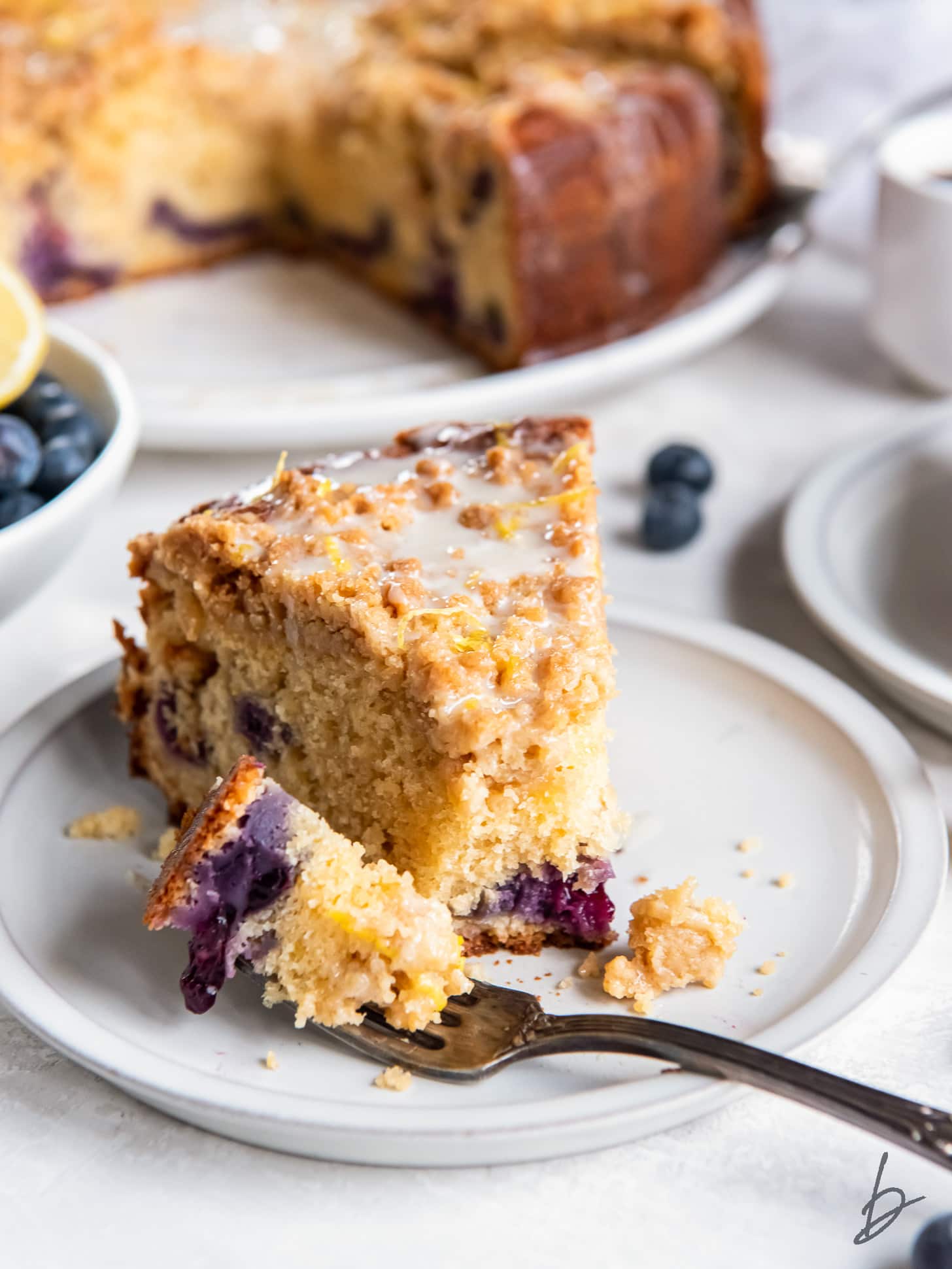 fork holding bite of blueberry buckle coffee cake on plate.