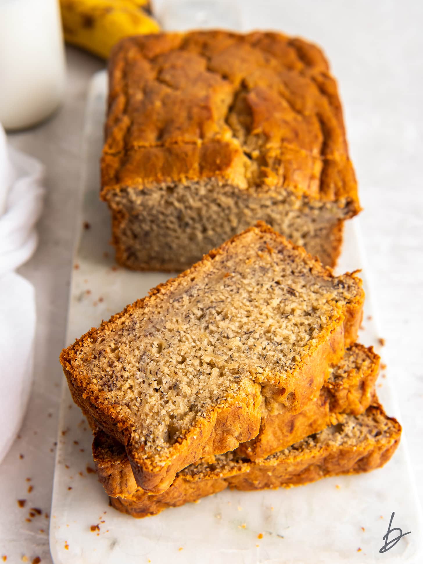 stack of banana bread slices on marble serving board in front of loaf.