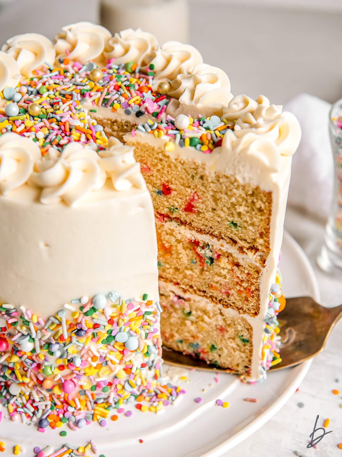 cake server pulling slice of cake out of three layer funfetti cake with frosting and sprinkles.