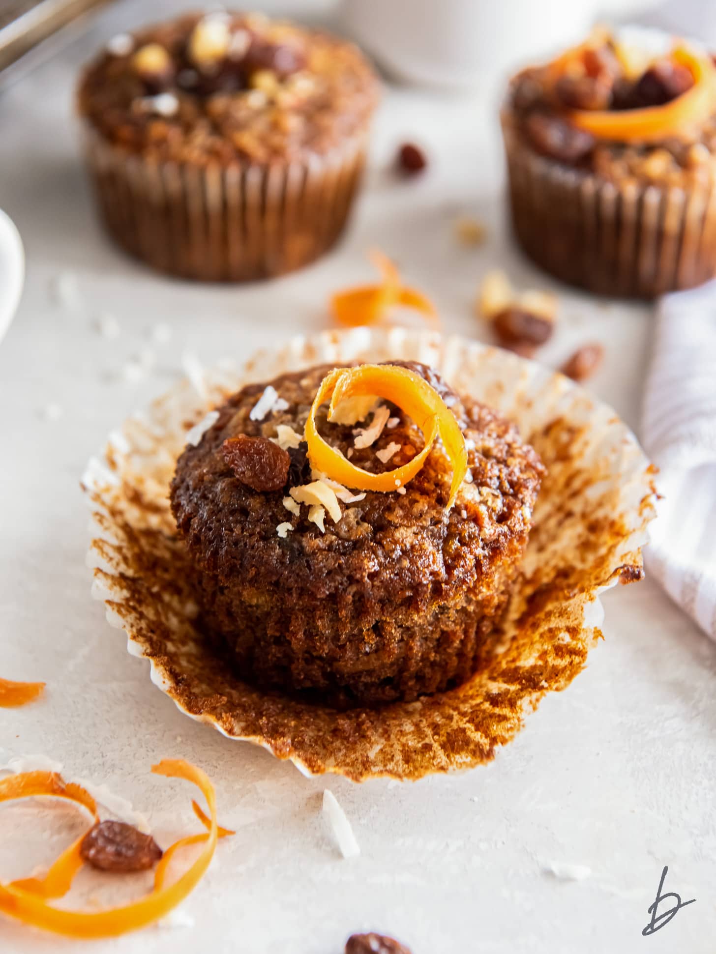 morning glory muffin on an open paper liner with a shred of carrot as garnish.