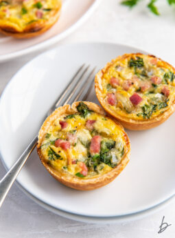 two muffin tin quiches on a white plate with a fork.