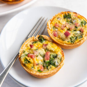 two muffin tin quiches on a white plate with a fork.