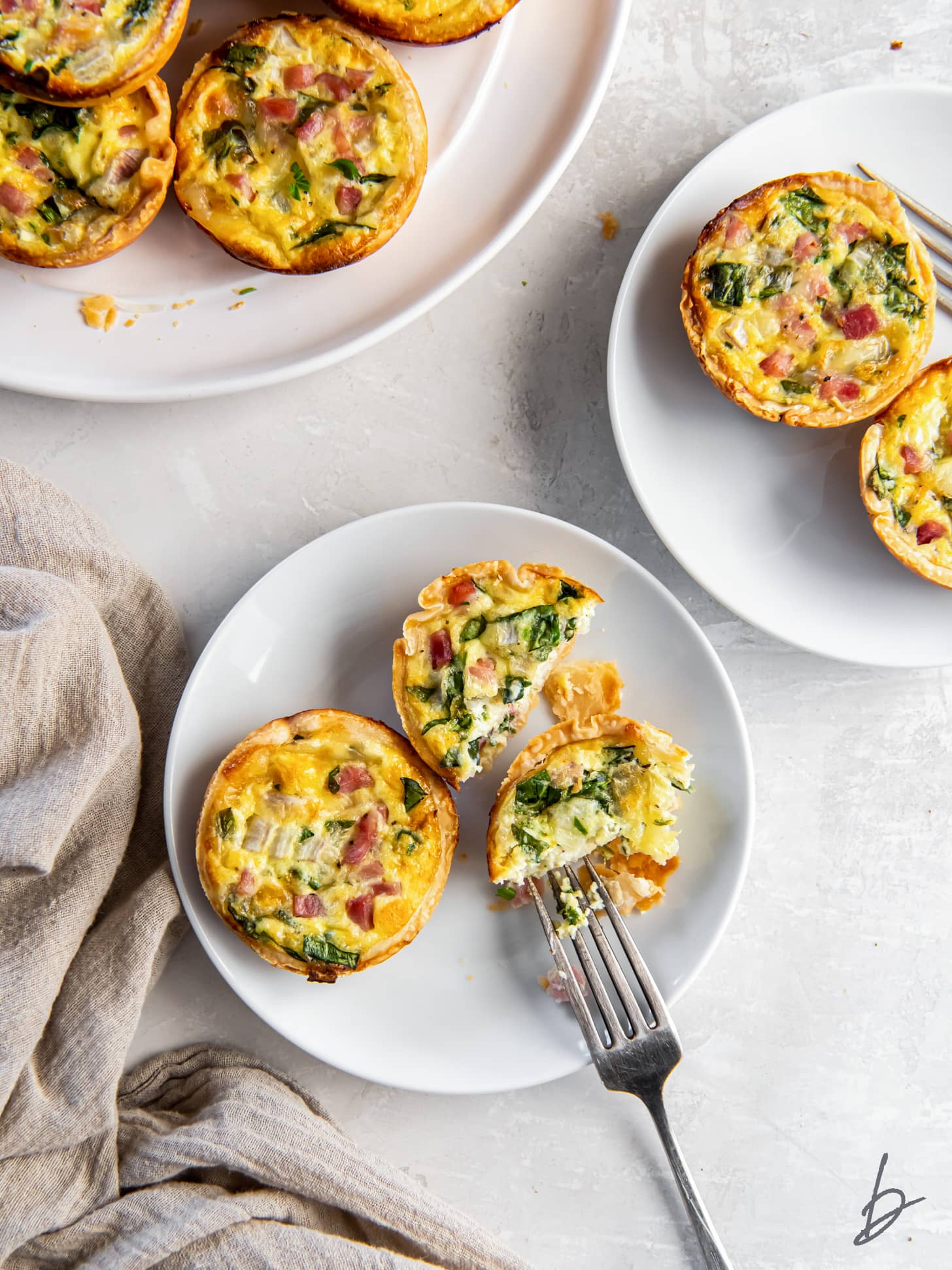 fork taking bite of mini quiche on a plate with a few more quiches.