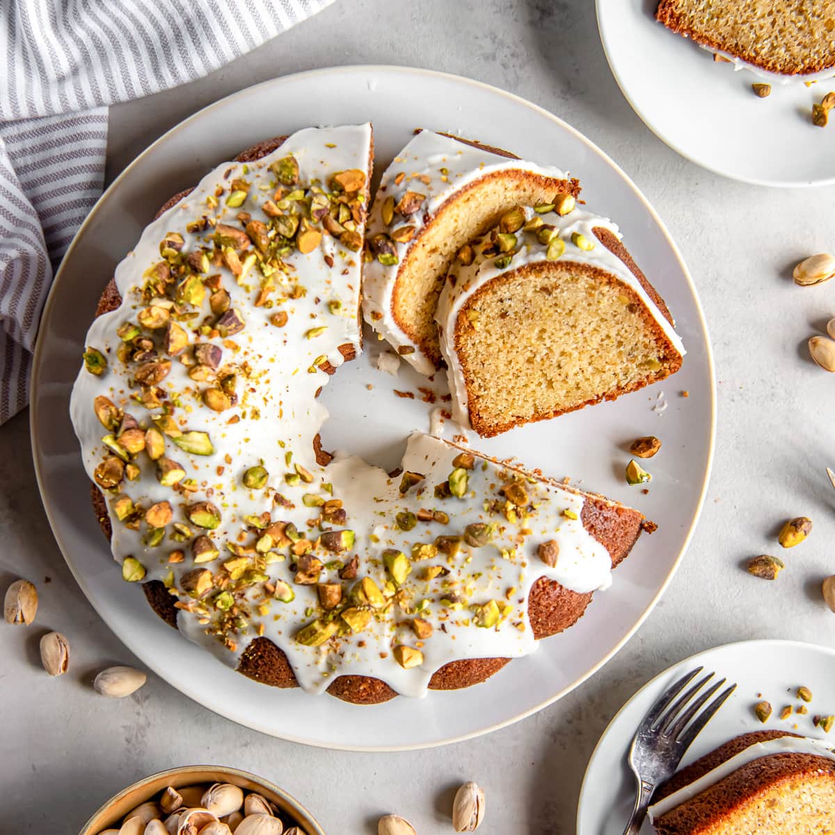 pistachio bundt cake with glaze and chopped pistachios on a plate with two slices cut.