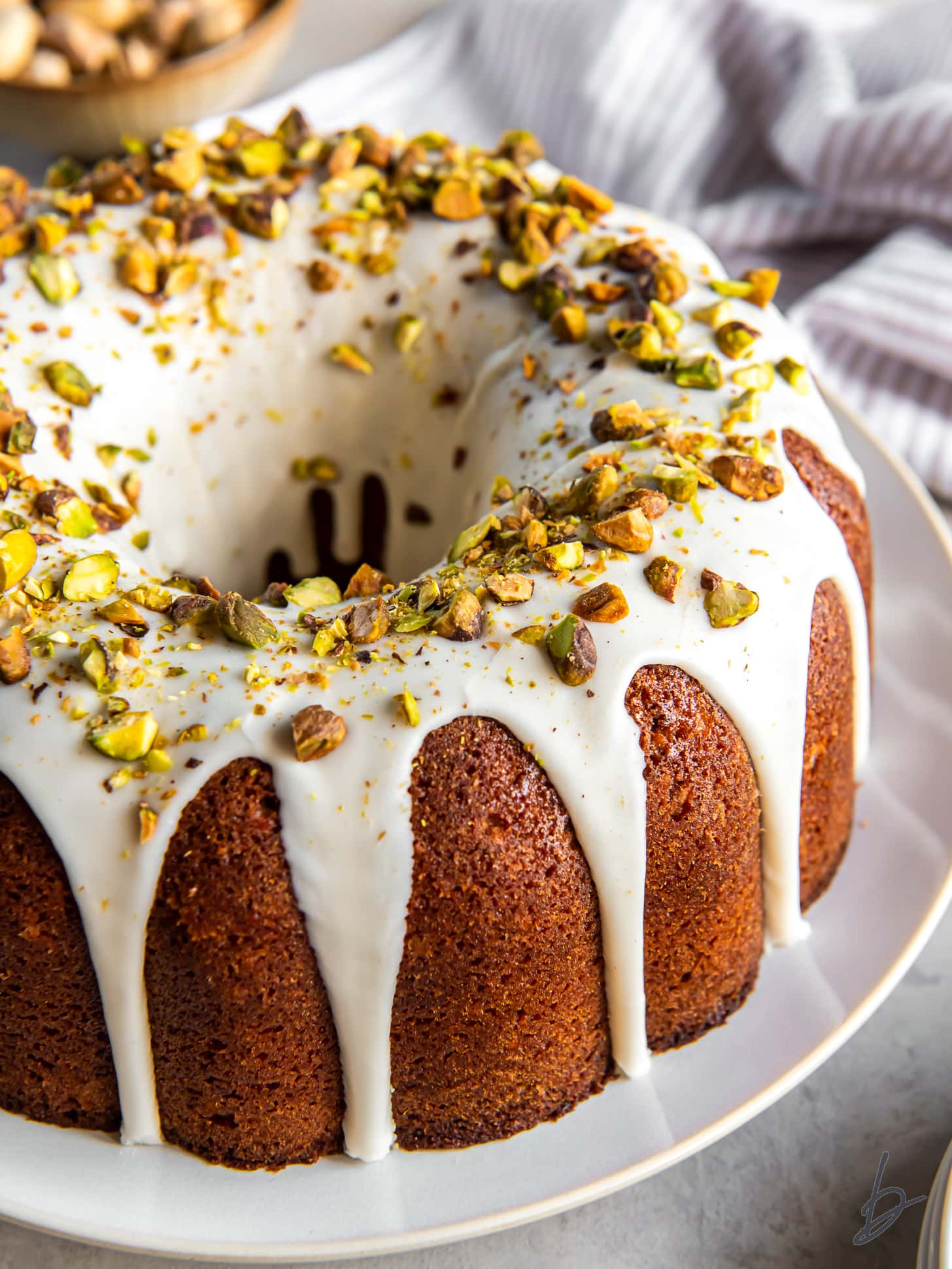 glaze dripping down sides of pistachio bundt cake garnished with chopped pistachios.