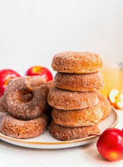 stack of five baked apple cider donuts on a plate with more donuts.