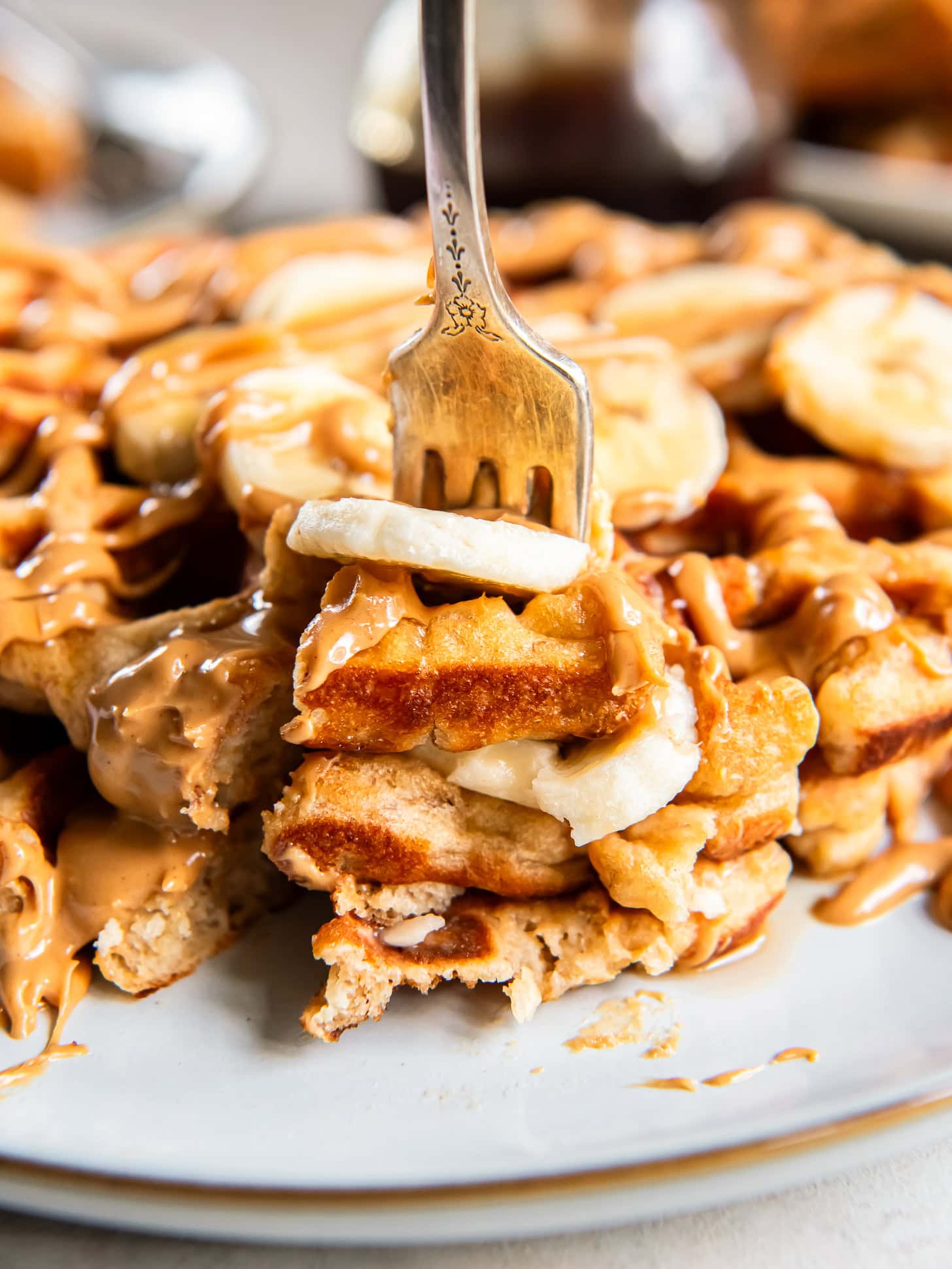 Fork holding bite of banana peanut butter waffles with fresh banana slices.