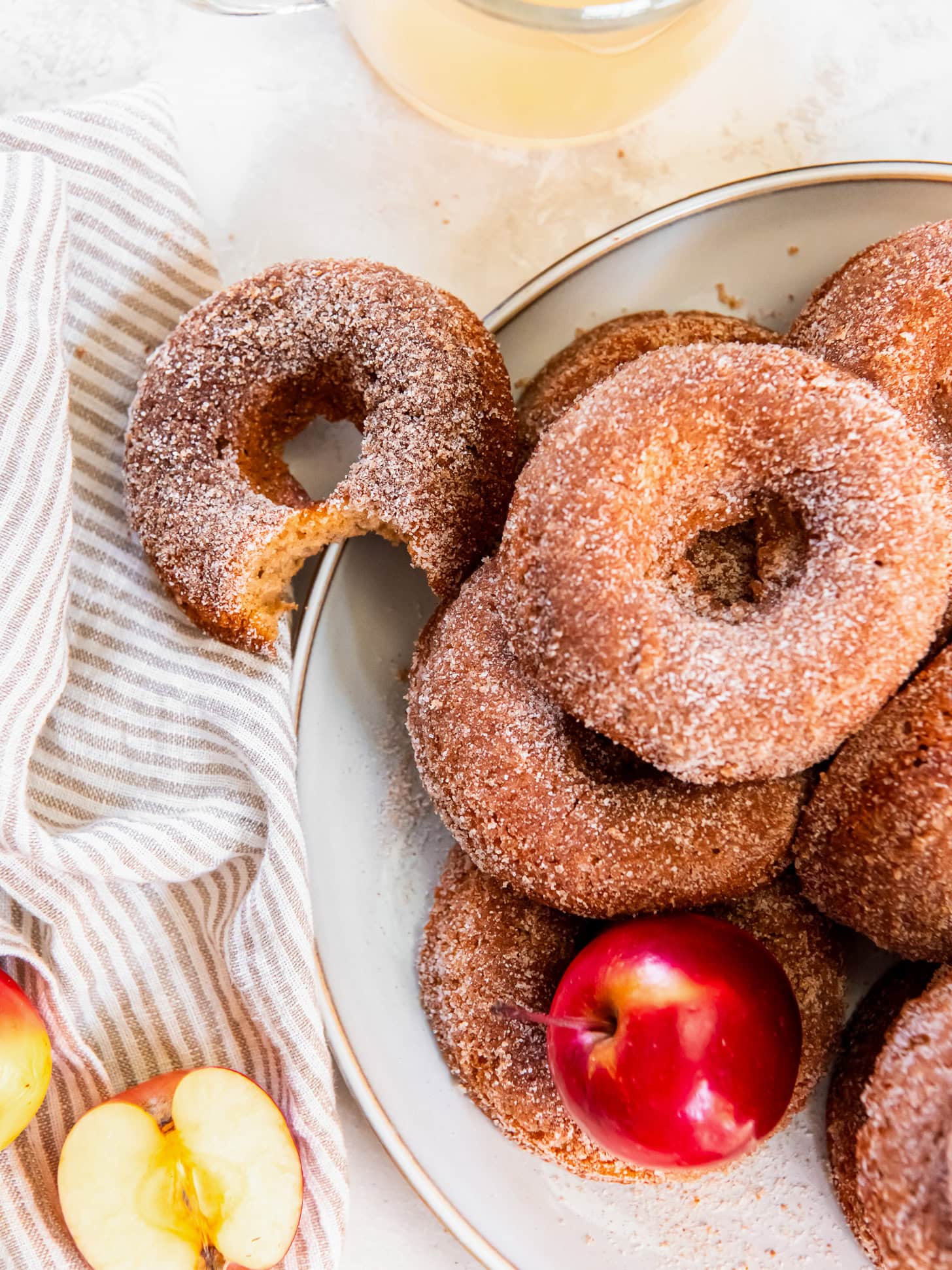 plate of apple cider donuts with cinnamon sugar coating and one donut has a bite.