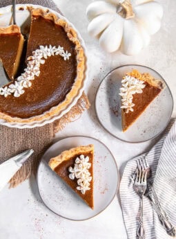 tabletop with pumpkin pie slices on two plates next to forks and the rest of the pie.