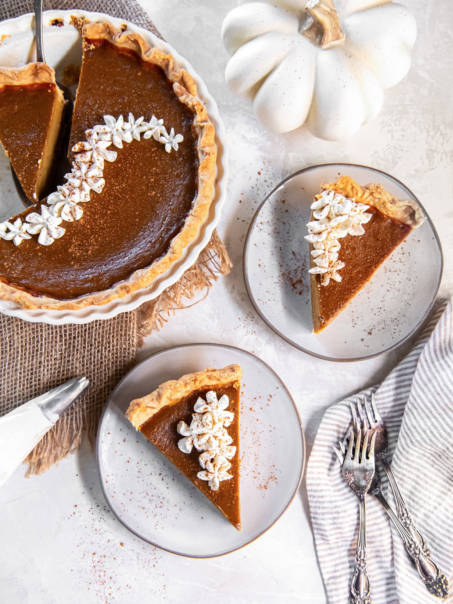 pumpkin pie slices on round plates with forks next to pie plate with remaining pie.