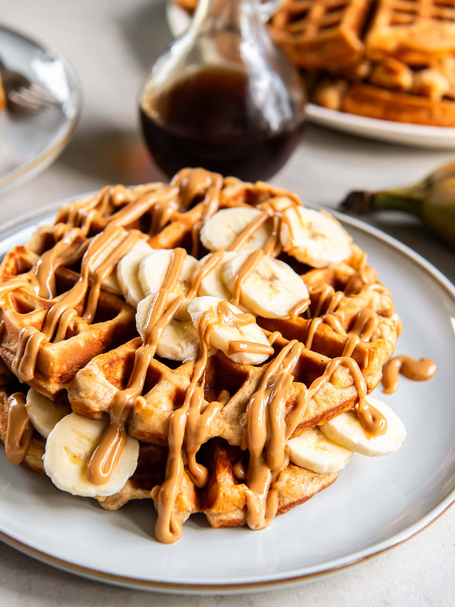 Stack of two peanut butter banana waffles on a plate with peanut butter drizzle and banana slices for garnish.