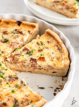 slice of quiche lorraine in white ceramic quiche pan.
