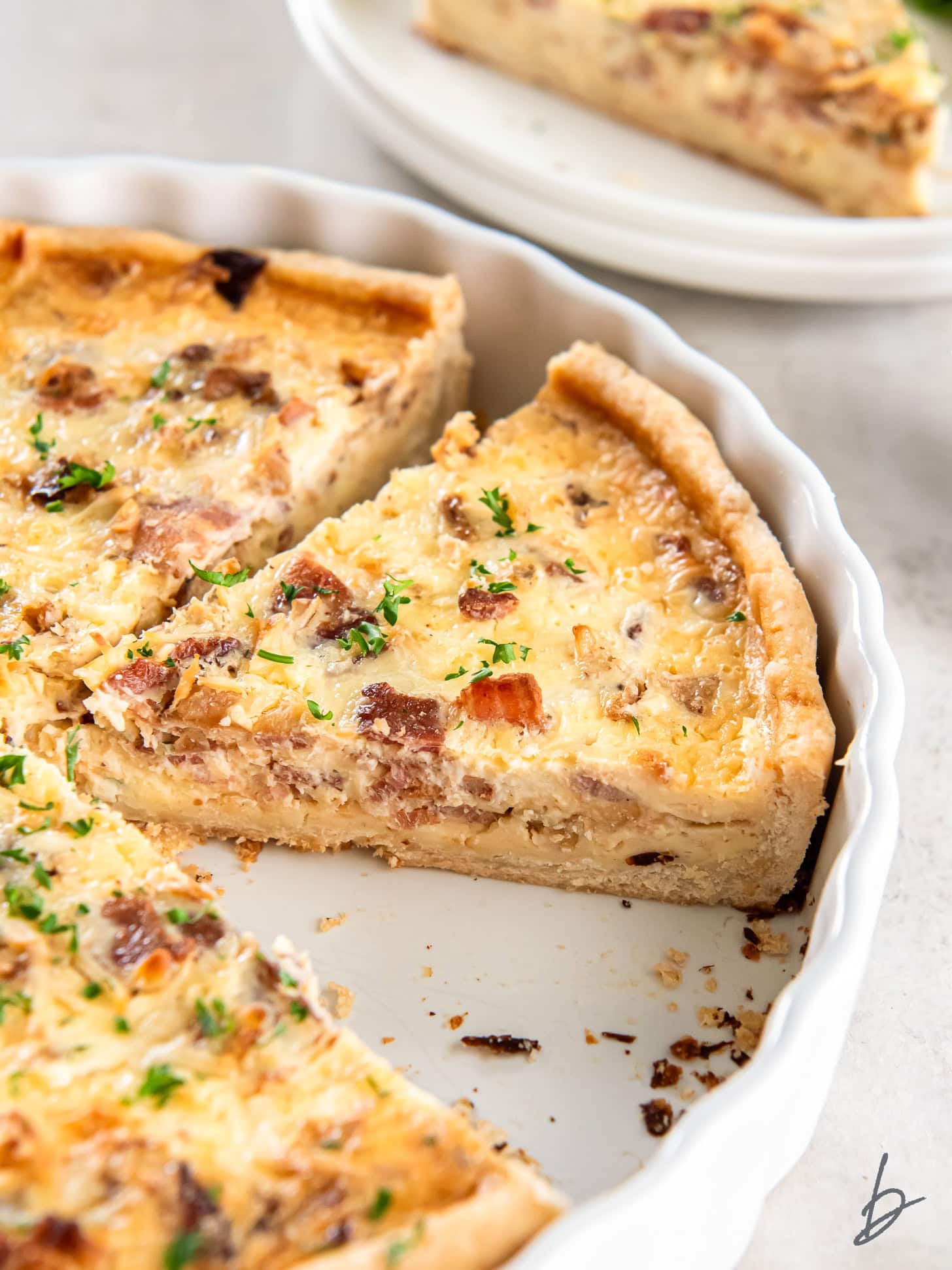 slice of quiche lorraine in white ceramic quiche pan.