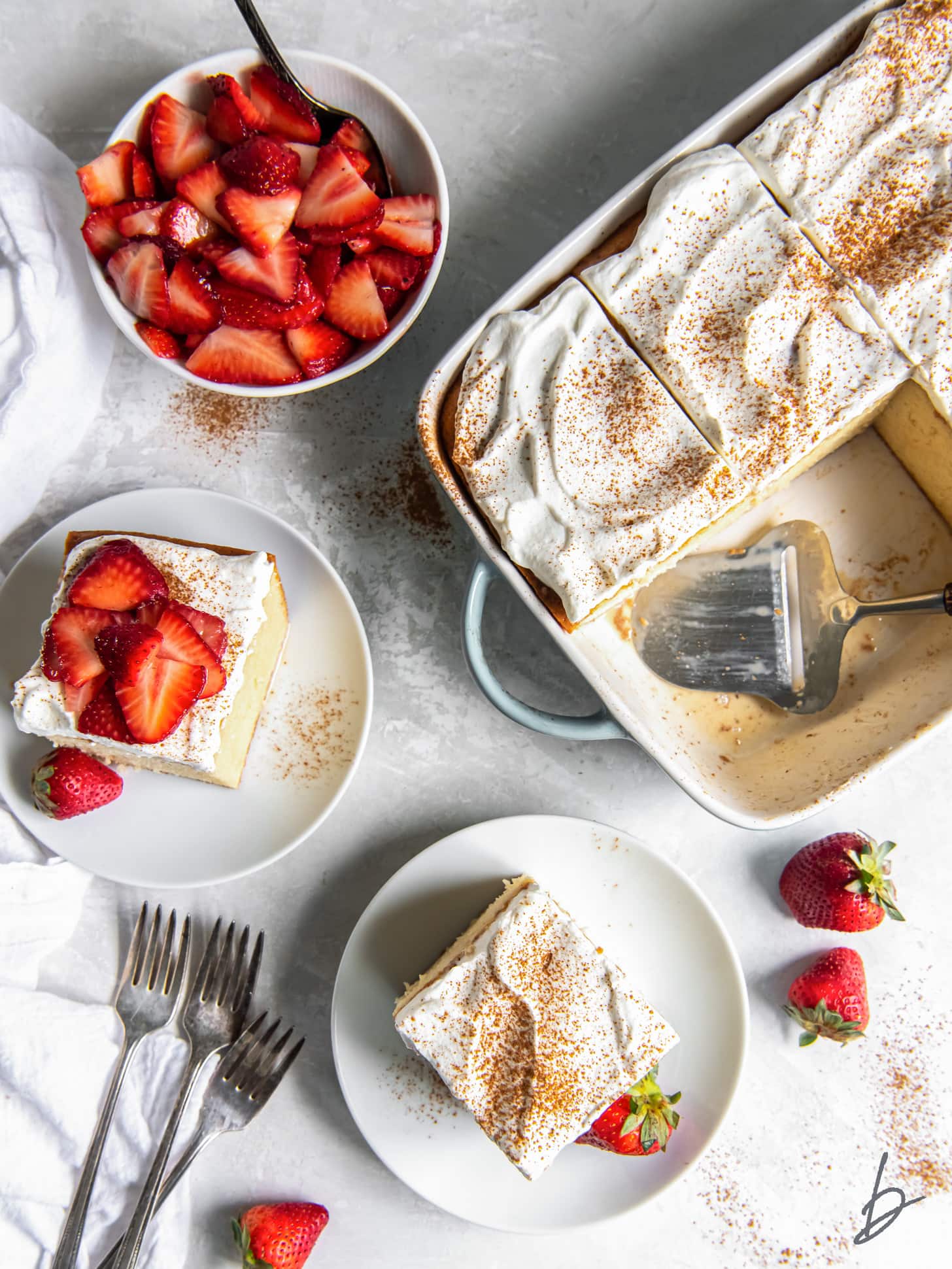 tres leches cake in a 9x13 pan next to slices of cake on small plates.