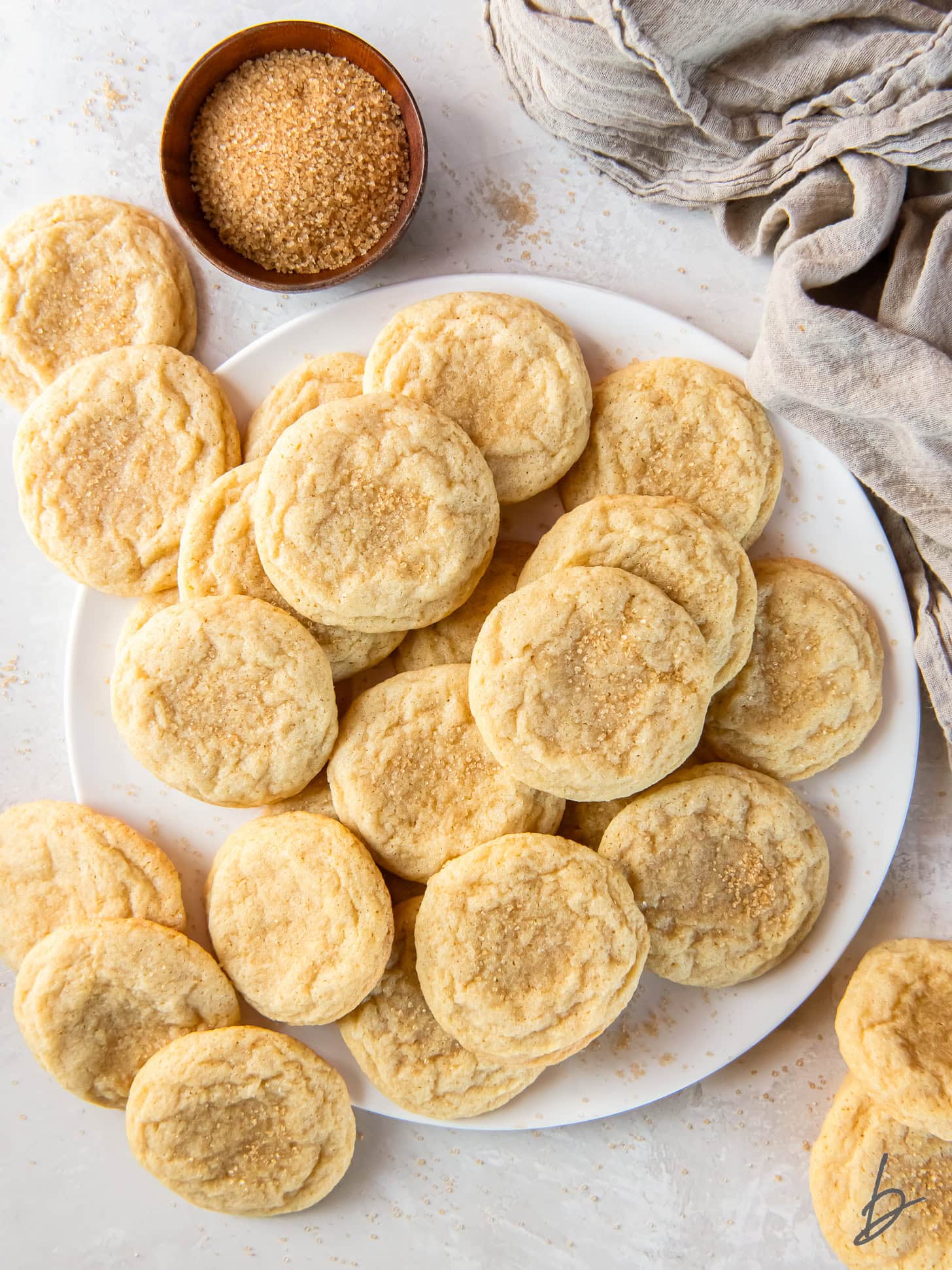 chewy sugar cookies on a plate on a tabletop with small bowl of turbinado sugar for garnish.