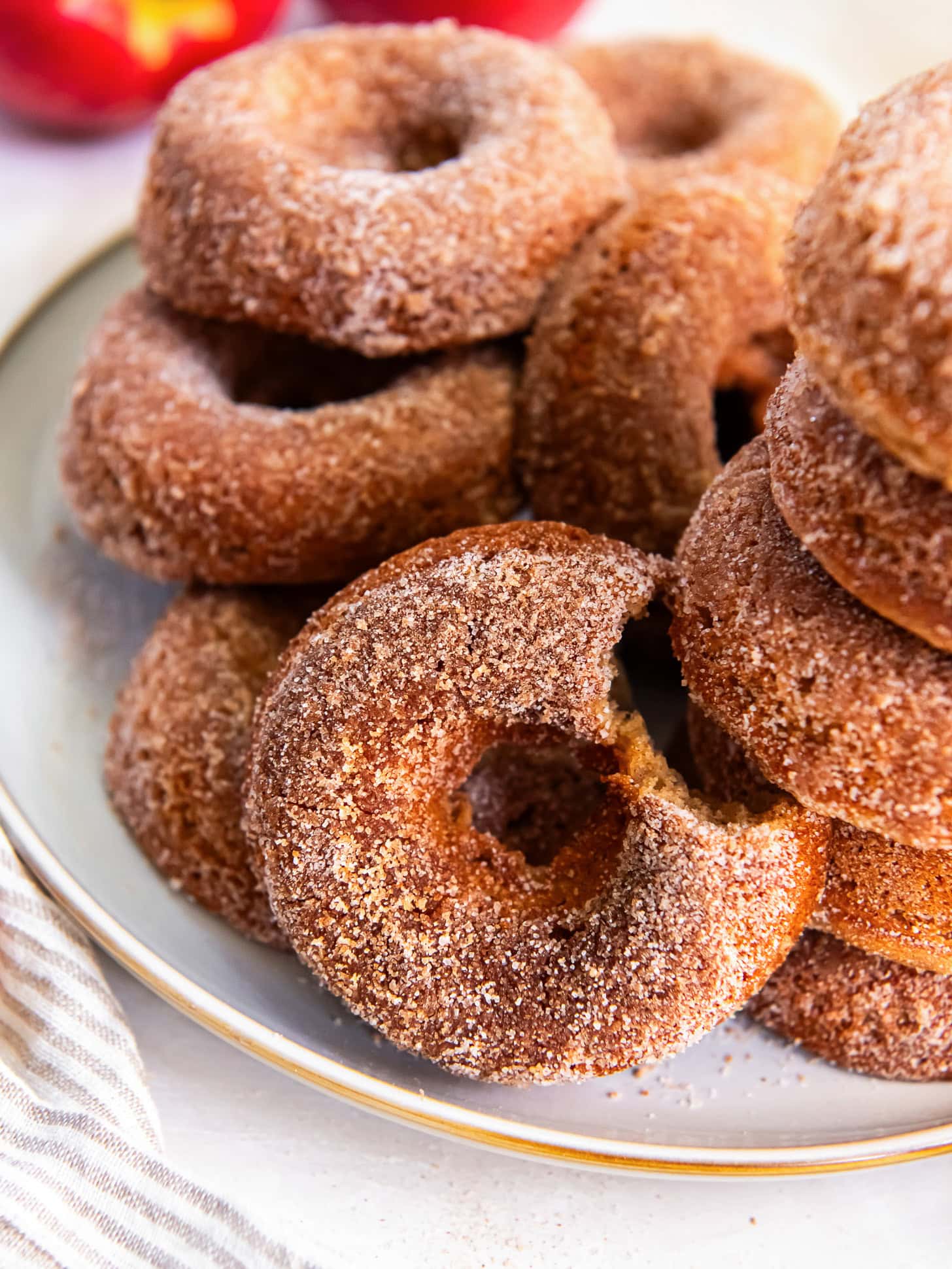apple cider donut with a bite leaning on more donuts on a plate.